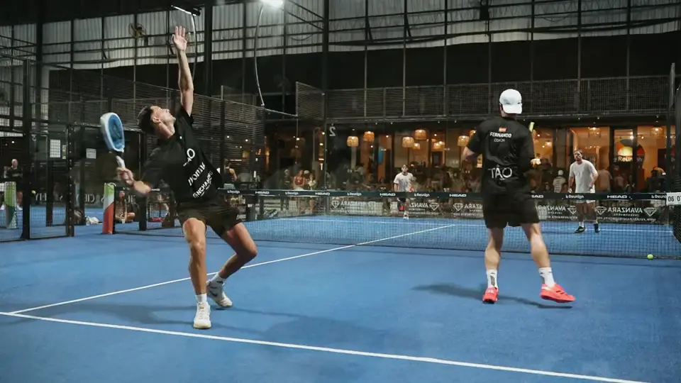 A player reaching low for a backhand on a blue padel court